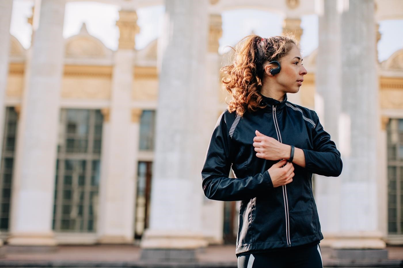 Portrait of young female athlete wearing sport jacket listening portable music player outdoors during the training session in the morning