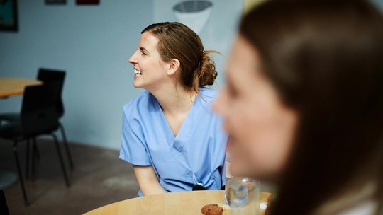 Smiling female medical workers looking away while sitting at table in hospital cafeteria