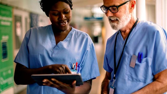 Two doctors man and woman looking at tablet smiling